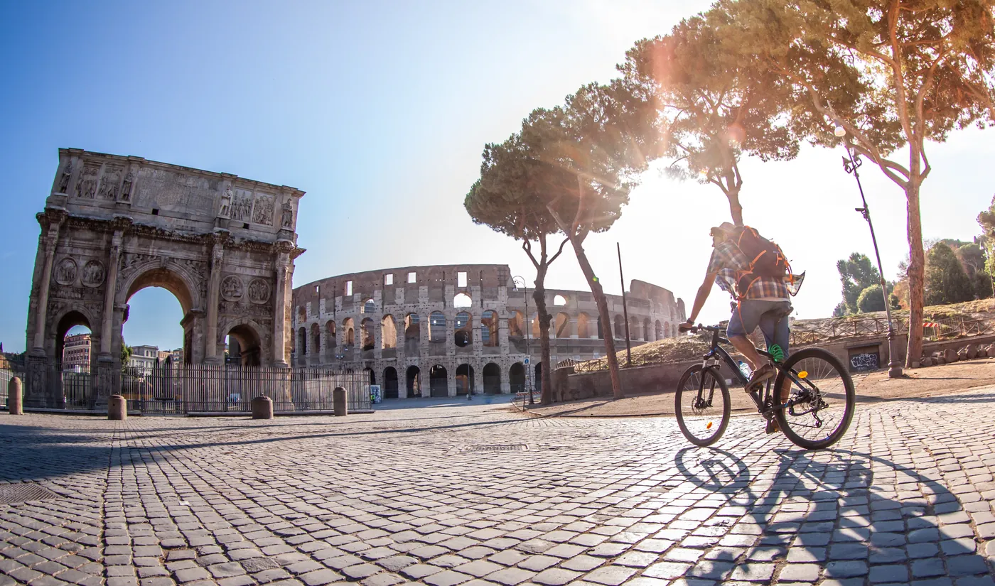 Cyclist riding cobblestones beside the Arch of Constantine and the Colosseum