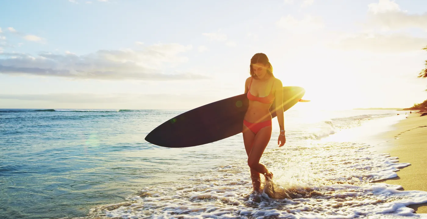 Woman carrying a surfboard along a sunny beach