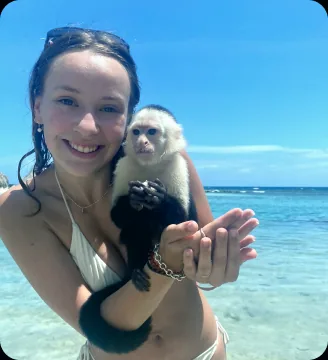 Person holding a white-faced capuchin on a tropical beach